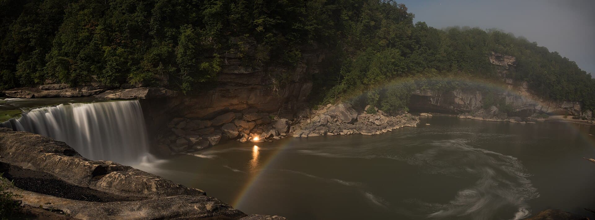 A pale moonbow arcing through mist below Cumberland Falls at night